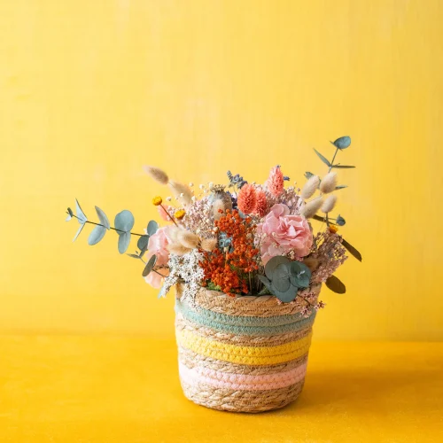 Centro en macetero de fibra natural con flores secas y preservadas de colores variados. Con hortensia rosa preservada